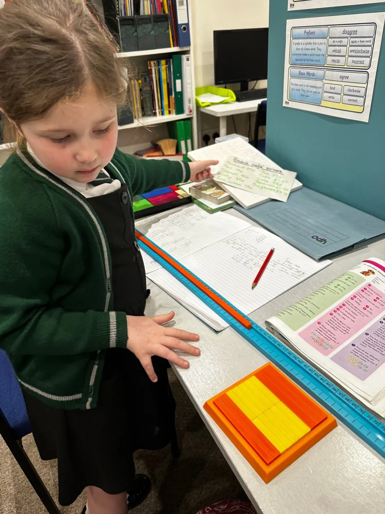 Primary pupil in school uniform working on money sums with Numicon and a ruler