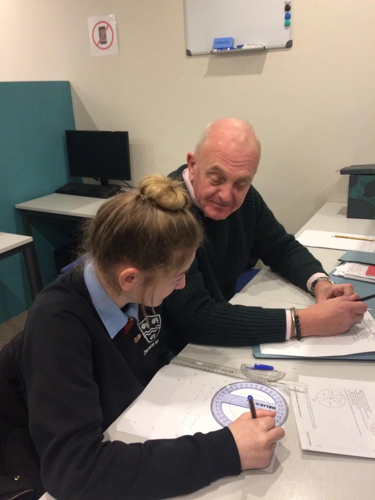 Tutor helping a secondary school student with maths at a desk