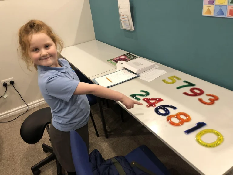 Young pupil pointing at a line of coloured jelly numbers on a desk