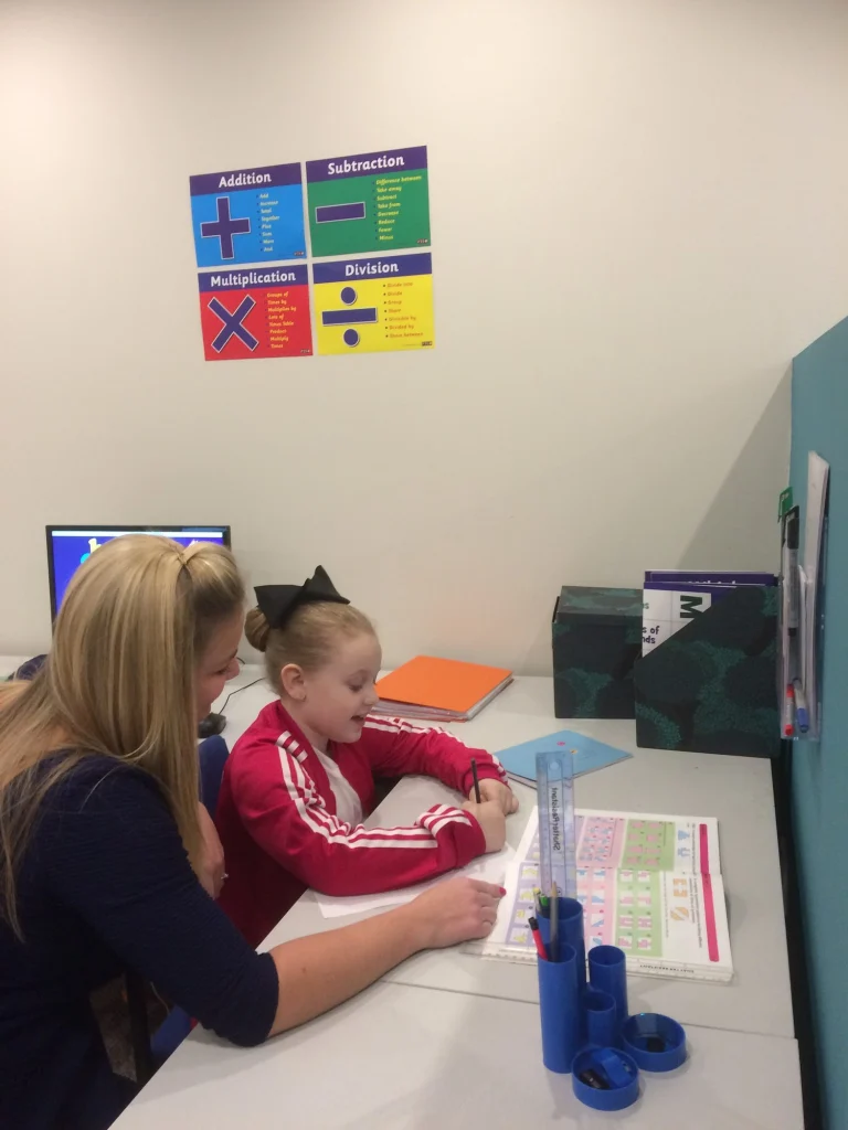 Tutor supporting a young girl with her work at a desk