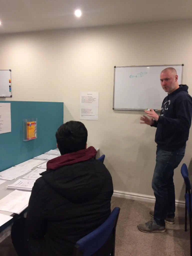 Tutor teaching at a whiteboard while a student works