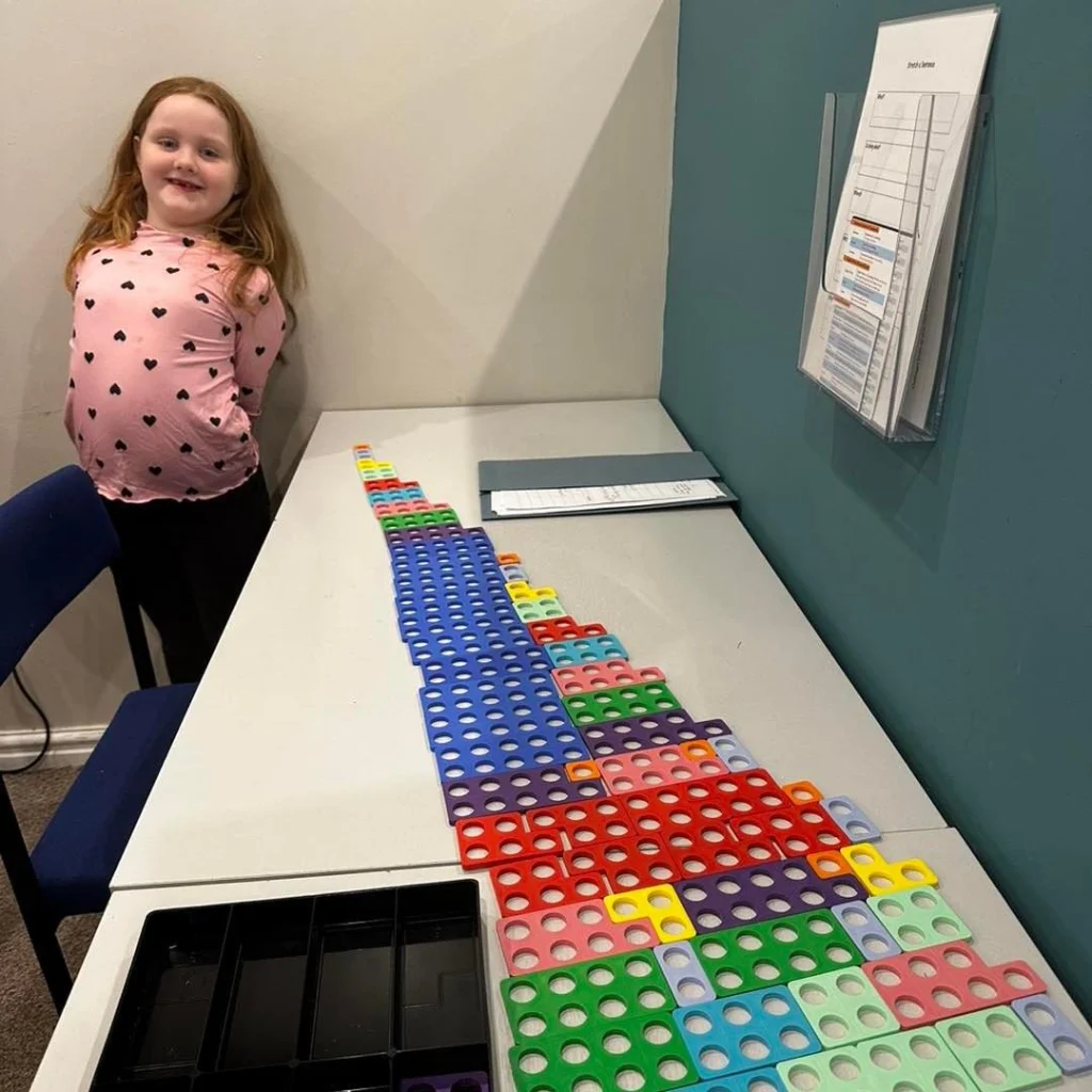 Pupil standing beside a long staircase of Numicon shapes on a table