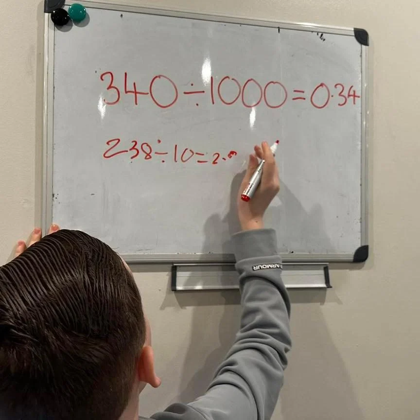 Student writing 340 divided by 1000 = 0.34 on a whiteboard