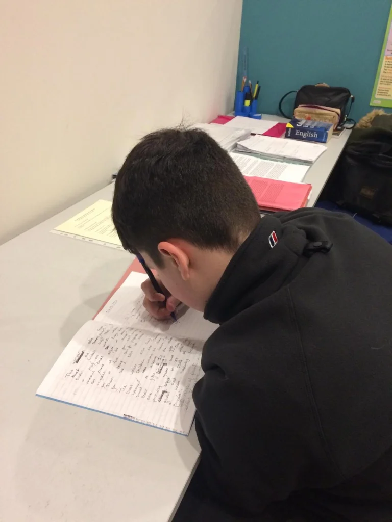 Secondary student writing in an exercise book at a desk
