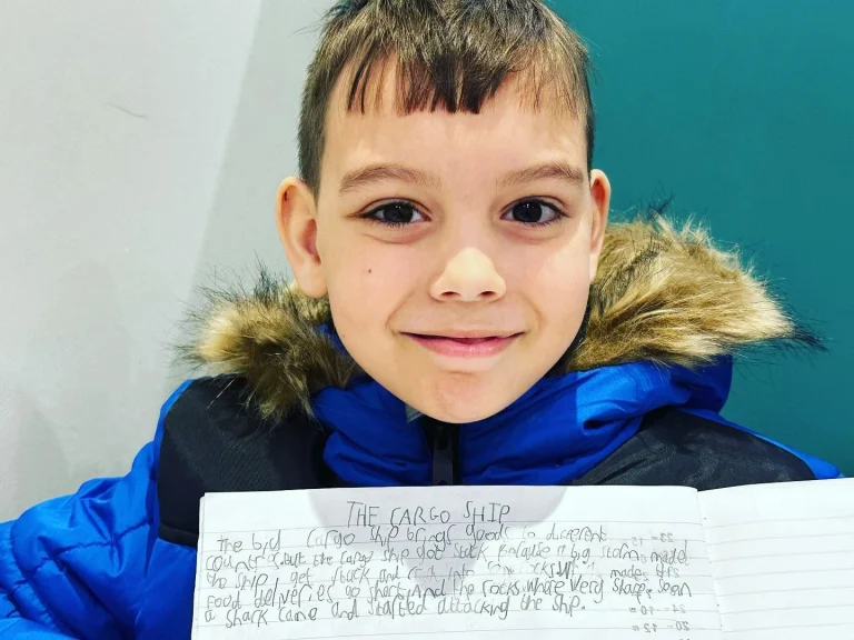 Smiling boy holding his handwritten story The Cargo Ship